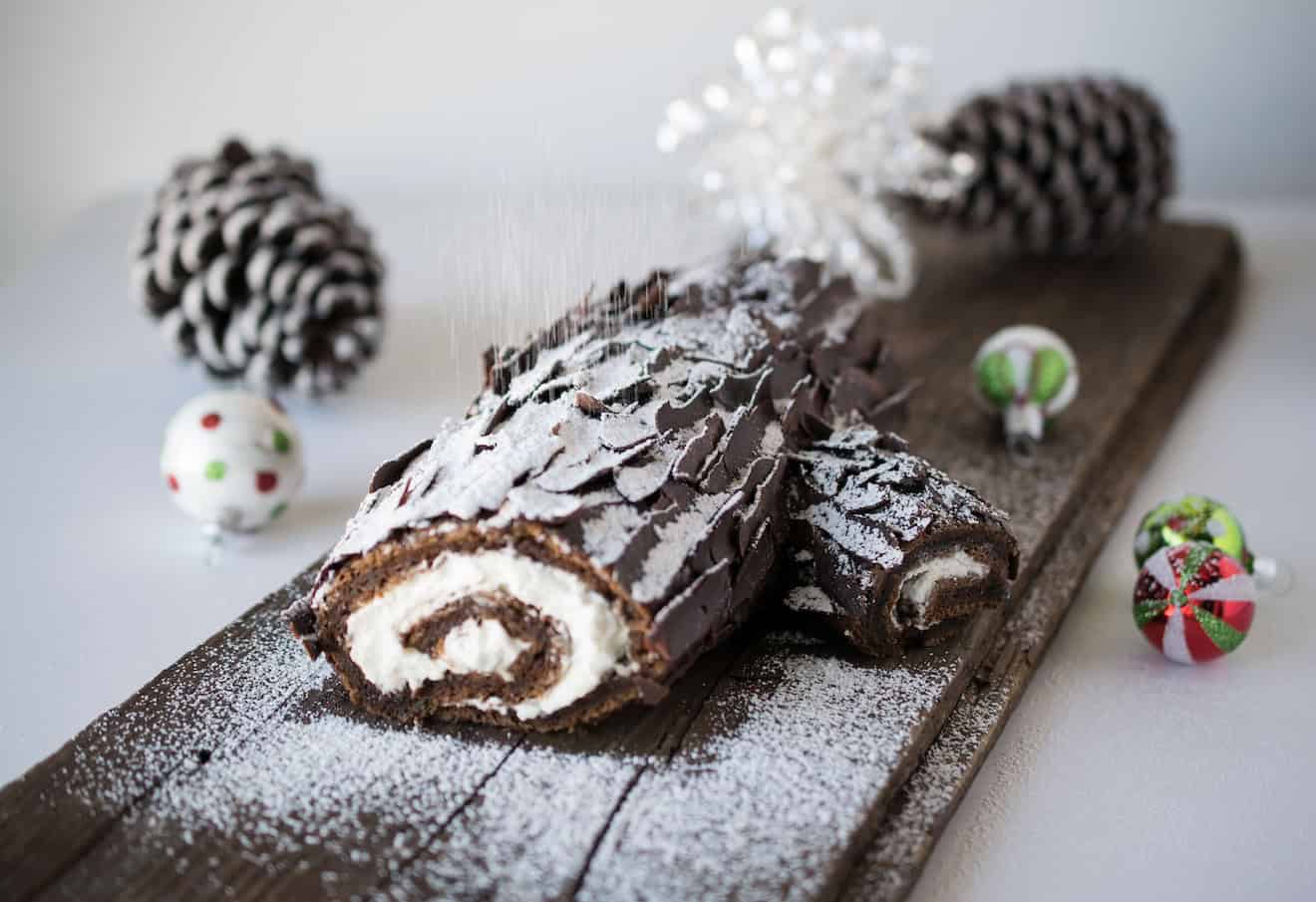 The side view of a chocolate yule log showing the cream filling and dusting of powdered sugar falling like snow