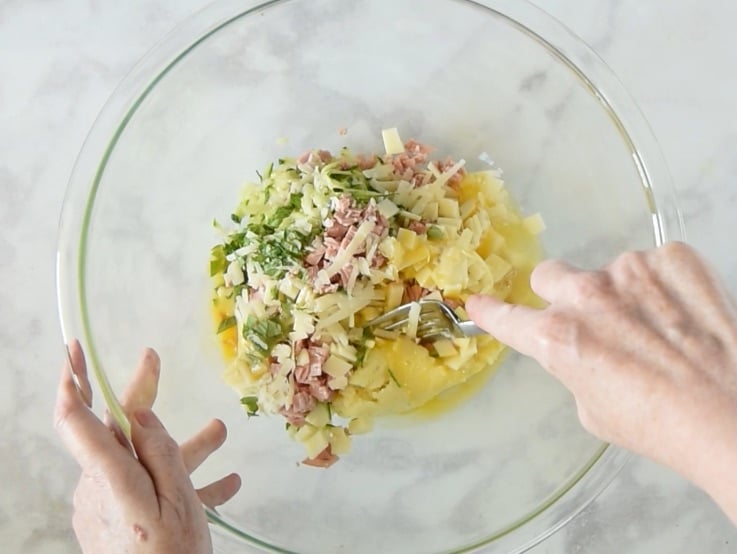 Mashed potato, zucchini, mortadella, provolone, parmesan, basil and egg are mixed in a glass bowl