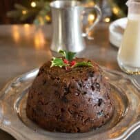 A dark brown Christmas pudding on a plate with brandy sauce