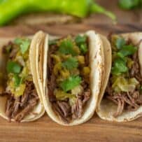 3 Sonoran shredded beef tacos on a board with hatch chile sauce and cilantro